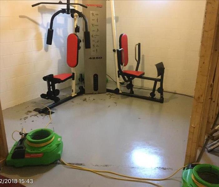 Exercise equipment in the corner of the basement with air movers in front of it