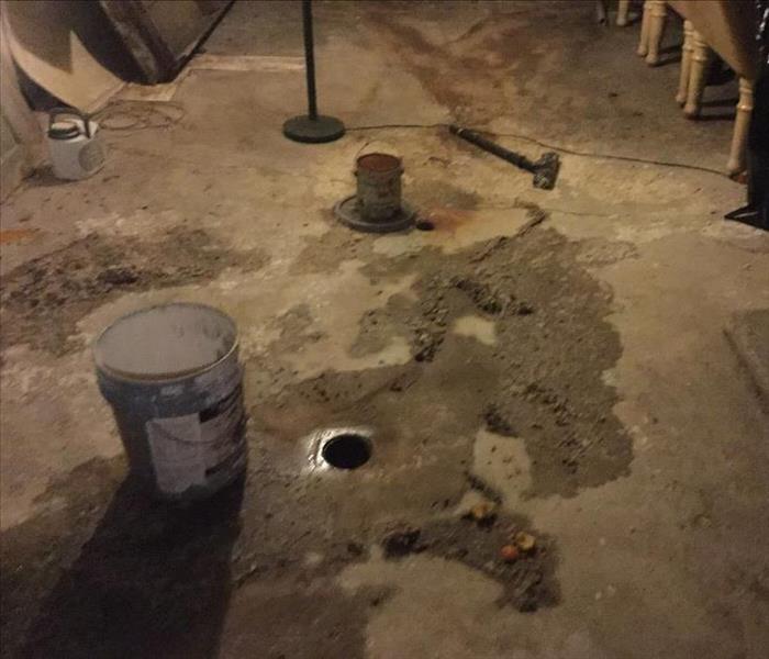 Unfinished basement with dirty water and debris on the floor with a floor drain