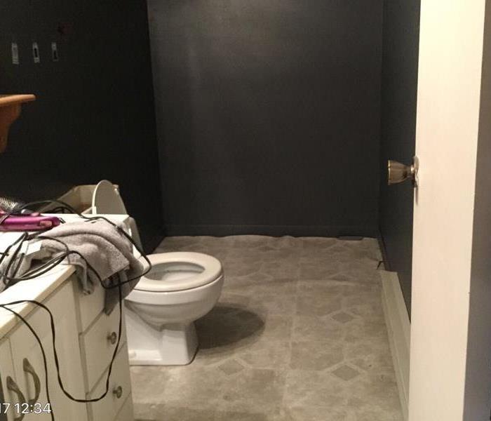 Bathroom with dark gray walls and white toilet and cabinet with light gray flooring coming up along the wall