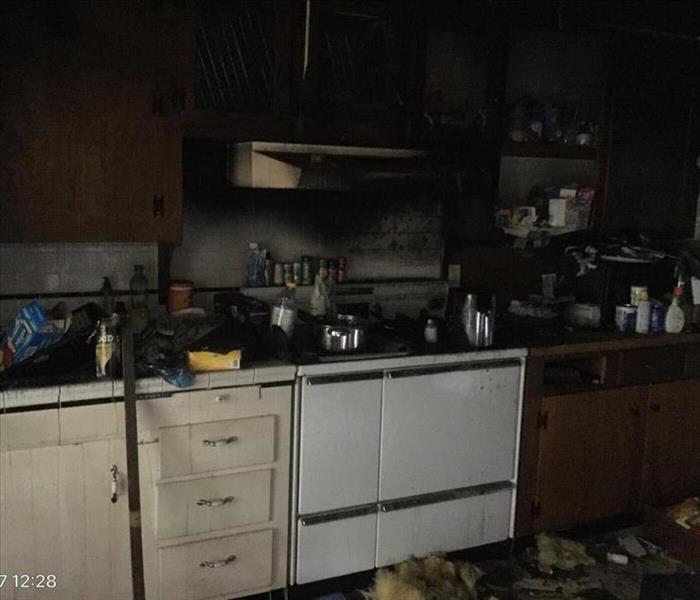 White stove and white and wood cabinets in a dark kitchen with soot and debris all over