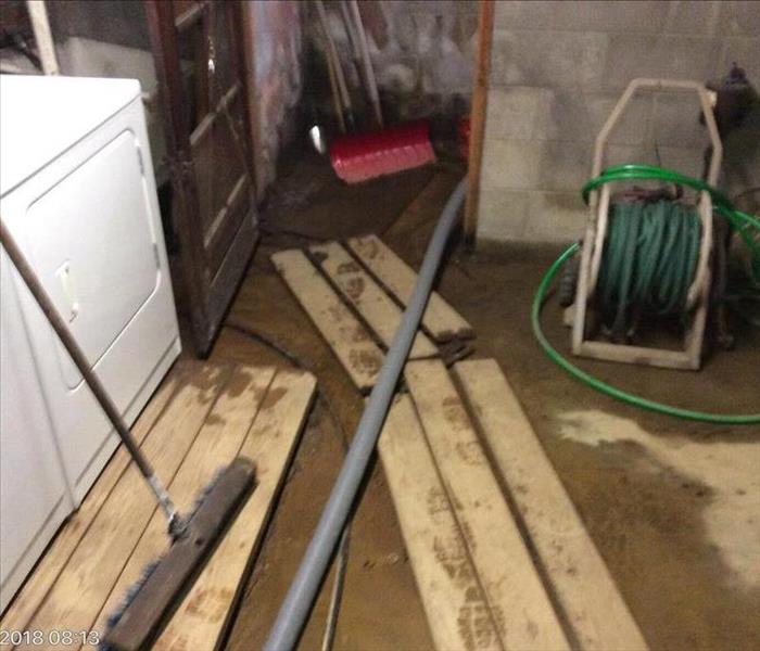 Washer and dryer in muddy basement with boards to walk over mud